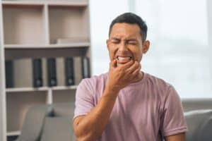 AdobeStock 658527076 - Viera Dental Arts | Dentist in Melbourne FL Middle-aged Asian Indian man with gum disease, toothache, wisdom tooth and molar pain. sitting on the sofa
