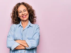 AdobeStock 354110985 - Viera Dental Arts | Dentist in Melbourne FL Middle age beautiful woman wearing casual denim shirt standing over pink background happy face smiling with crossed arms looking at the camera. Positive person.